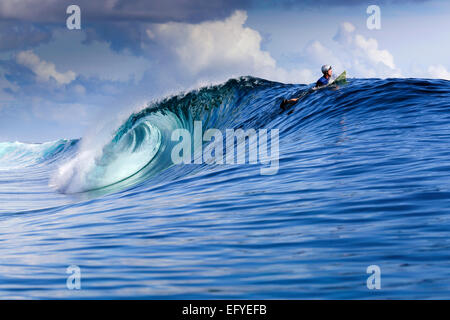Surfer wearing helmet paddles over large surfing wave in the Maluku Islands, Indonesia Stock Photo