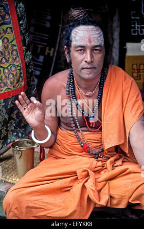 A younger holy man wearing saffron-colored clothing makes a spiritual hand gesture outside a Hindu temple in Kathmandu, Nepal, in South Asia. Stock Photo