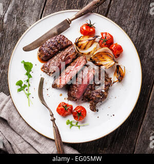 Sliced medium rare grilled Beef steak Ribeye with grilled onions and cherry tomatoes on plate on wooden background Stock Photo