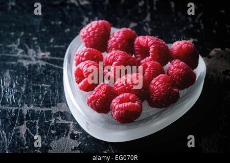 Fresh raspberry in heart shaped plate over black wooden background. Stock Photo
