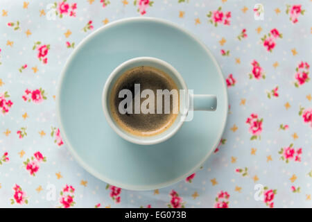 Espresso coffee in a blue cup and saucer on a floral table cloth. Stock Photo