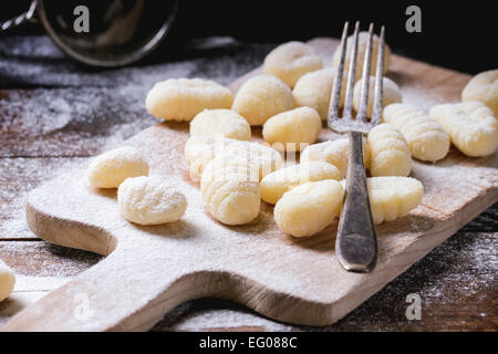 Uncooked homemade potato gnocchi with fork and strainer on vintage cutting board over wooden table with flour. See series Stock Photo