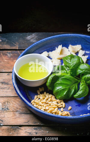 Ingredients for basil pesto served on blue ceramic plate over old wooden table. Stock Photo