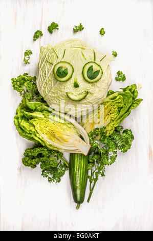funny girl face made of  green vegetables, cucumber and lettuce on white wooden background Stock Photo