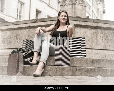 Photo of a beautiful young woman sitting at a fountain in an old European city resting from shopping. Stock Photo