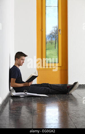 Photo of a young student reading a book in the hallway of his school. Stock Photo