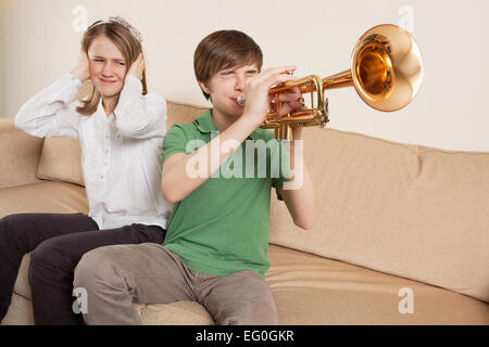 Photo of a brother playing his trumpet too loudly, or badly, and annoying his sister. Stock Photo