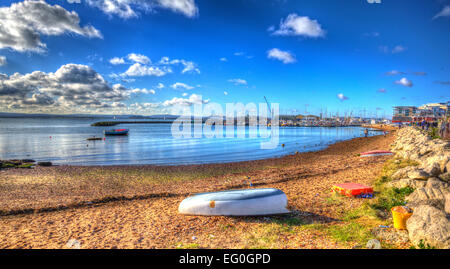 Wooden rowing boat and view towards Poole harbour and quay Dorset England UK in vivid colourful HDR with sea lapping on the sand Stock Photo