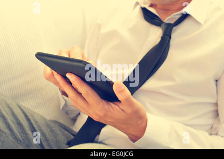 a relaxed young man with his necktie loosened using a tablet computer Stock Photo