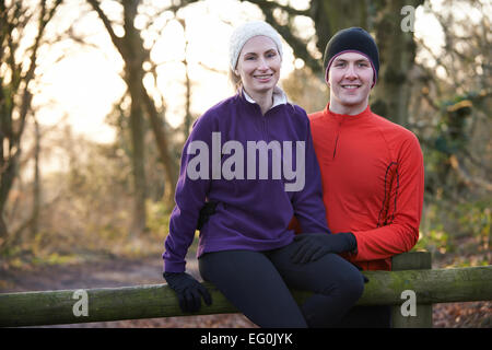 Portrait Of Couple On Winter Run Through Woodland Sitting On Fence