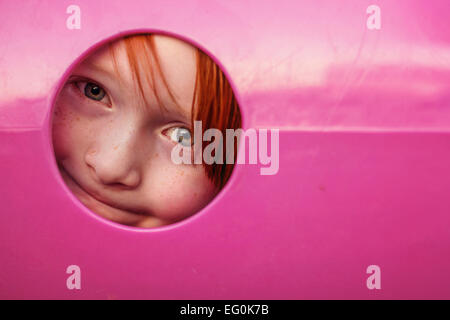 Young boy peeking through hole in playground tunnel Stock Photo