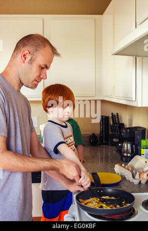 Two boys helping their father make eggs for breakfast Stock Photo