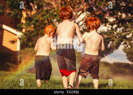 Three young brothers playing in water sprinklers Stock Photo