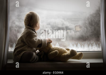 Boy sitting on window sill with teddy bear