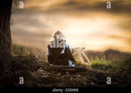 Rear view of boy sitting by a tree with his teddy bear Stock Photo