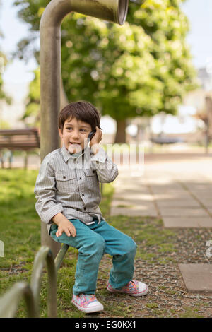 Bulgaria, Sofia, Boy (4-5) sitting on park railing talking on mobile phone Stock Photo