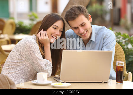 Happy couple watching social media in a laptop in a restaurant terrace Stock Photo