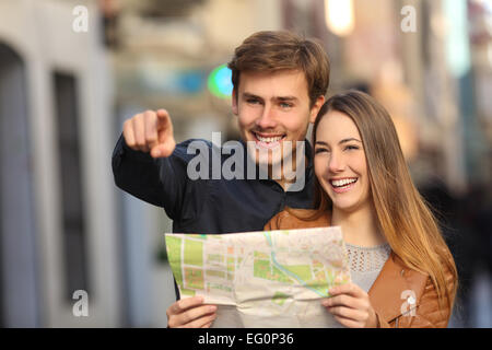 Happy couple of tourists on vacations searching a street in a map and pointing away Stock Photo