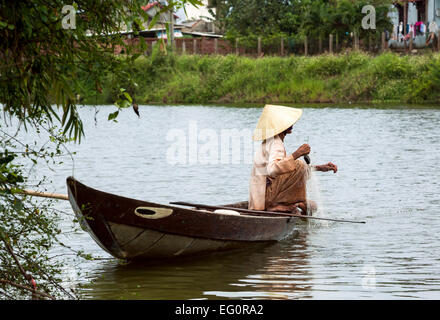 Traditionally dressed old woman fishing from her small fishing boat, Hoi An, Vietnam, Indochina, Southeast Asia, Asia. Stock Photo