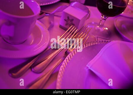 table setting at a wedding reception showing forks cups and plates bathed in purple light Stock Photo