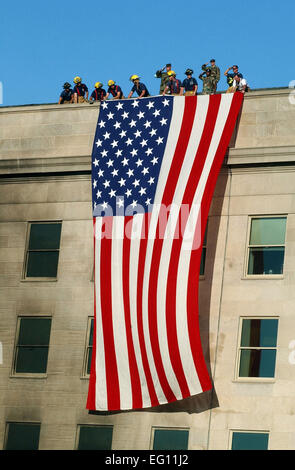 Military members rendered honors as fire and rescue workers unfurled a huge American flag over the side of the Pentagon Sept. 12, 2001, during rescue and recovery work following the Sept. 11 terrorist attack. The attack came at approximately 9:40 a.m. as a hijacked commercial airliner, originating from the Dulles International Airport in Washington, D.C., was flown into the southern side of the building facing Virginia Highway 27.  by Michael W. Pendergrass Stock Photo