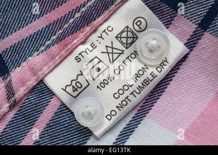 label showing washing instructions in 100% cotton check shirt with spare buttons - Care washing symbols and instructions Stock Photo