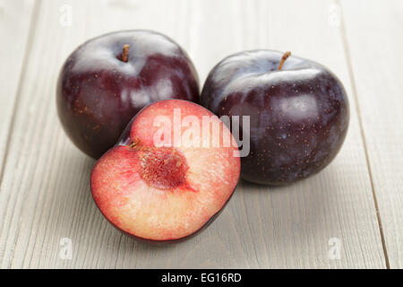three ripe black plums on wood table Stock Photo