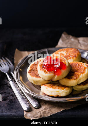 Cottage cheese pancakes with currant jam on vintage metal plate, selective focus Stock Photo