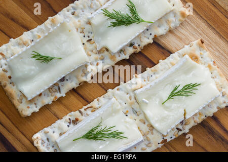 close up of slices of brie cheese on everything crackers with fresh dill Stock Photo