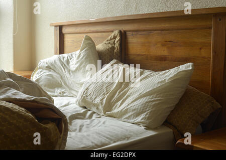 An unmade double bed with wooden headboard Stock Photo