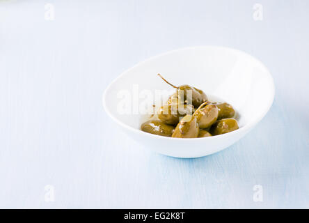 Green olives marinated with coriander in white bowl on light blue background, copy space, selective focus Stock Photo