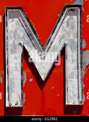 Vintage, run-down, antique letter 'M' on a red, flaky painted background Stock Photo