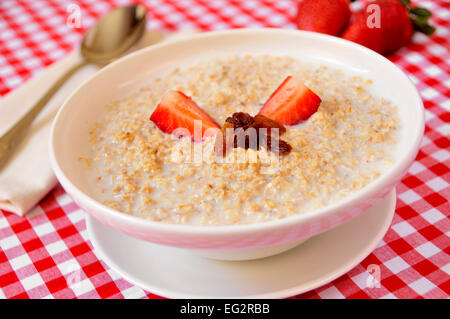 closeup of a bowl with porridge with sultana raisins and strawberry, on a set table for breakfast Stock Photo