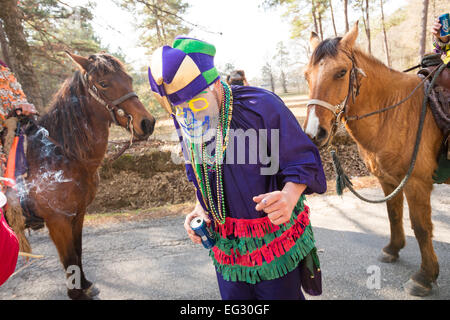 Wearing traditional Cajun Mardi Gras costume and mask runners dance in the streets during the Courir de Mardi Gras February 14, 2015 in Elton, Louisiana. Revelers go from house to house begging to gather food for a communal meal and celebrate by dancing for bystanders when successful. Capitaines riding horseback try to control the good natured revelers as they romp through the countryside causing mischief. Stock Photo