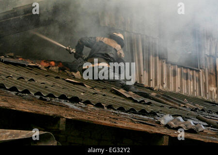 Smoldering remains of a ghetto house with a fireman spraying water firefighters extinguish a fire in an apartment house Stock Photo