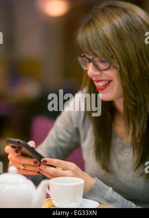 Beautiful young woman checking her mobile phone whilst having a hot drink a cosy cafe. Stock Photo