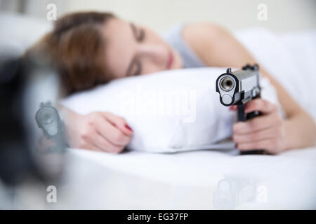 Woman in bed sleeps with hand on gun weapon home security. Focus on gun Stock Photo