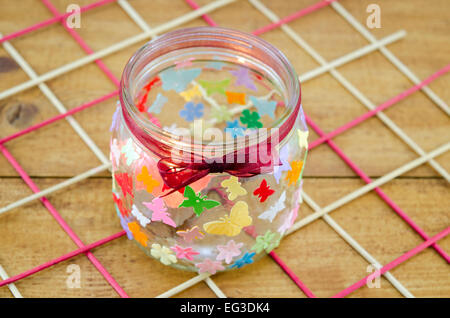 DIY candle holder decorated with colorful butterflies on a wooden table Stock Photo