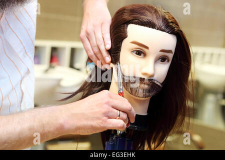 Barber student trimming brown hair using puppet and scissors Stock Photo