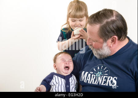 Sixty-one year old grandfather holding three month old grandson, with two year old, impish granddaughter looking amused Stock Photo