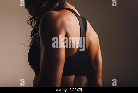 Fit and muscular woman in sports bra standing with her back towards camera. Rear view of fitness female with muscular body. Stock Photo