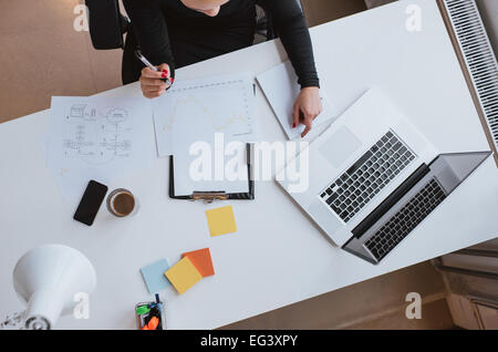 Top view of woman executive working at her desk with chart and laptop. Reviewing financial data and plotting progress thus far. Stock Photo
