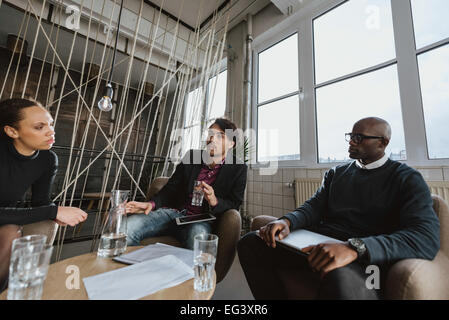 Group of multi ethnic executives discussing during a meeting in office lobby. Business people brainstorming ideas. Stock Photo