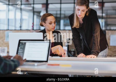 Shot of two coworkers going through paperwork together. Two young women reading a document while at a table in office. Stock Photo