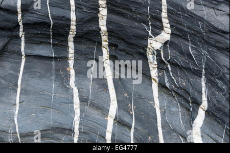 Black rock with different white stripes and little bit sand. Stock Photo