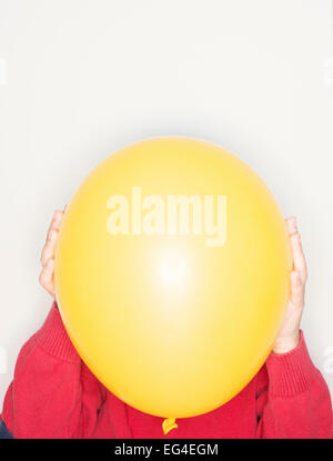 Child holding yellow balloon in front of face. Fun lifestyle moment. Stock Photo