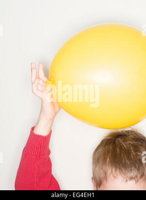 Child holding yellow balloon over hair. Fun childhood science experiment with electricity. Stock Photo