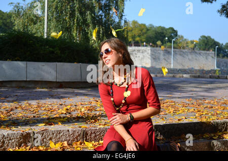 Young brunette in a red dress outdoors in autumn with yellow leaves falling Stock Photo