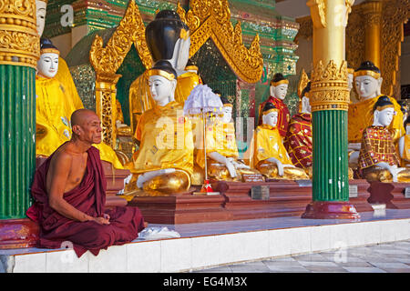 Buddhist monk praying in front of Buddha statues in the Shwedagon Zedi Daw Pagoda at Yangon / Rangoon, Myanmar / Burma Stock Photo