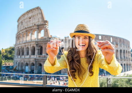 Happy young woman giving headphones with audio guide in front of colosseum in rome, italy Stock Photo